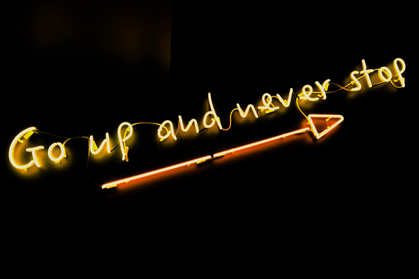 Yellow neon sign that says, "Go up and never stop."