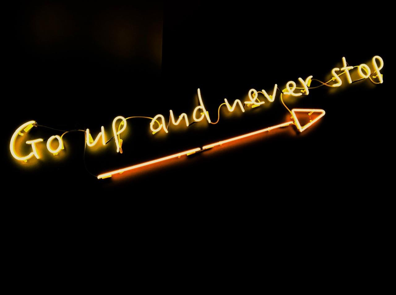Yellow neon sign that says, "Go up and never stop."