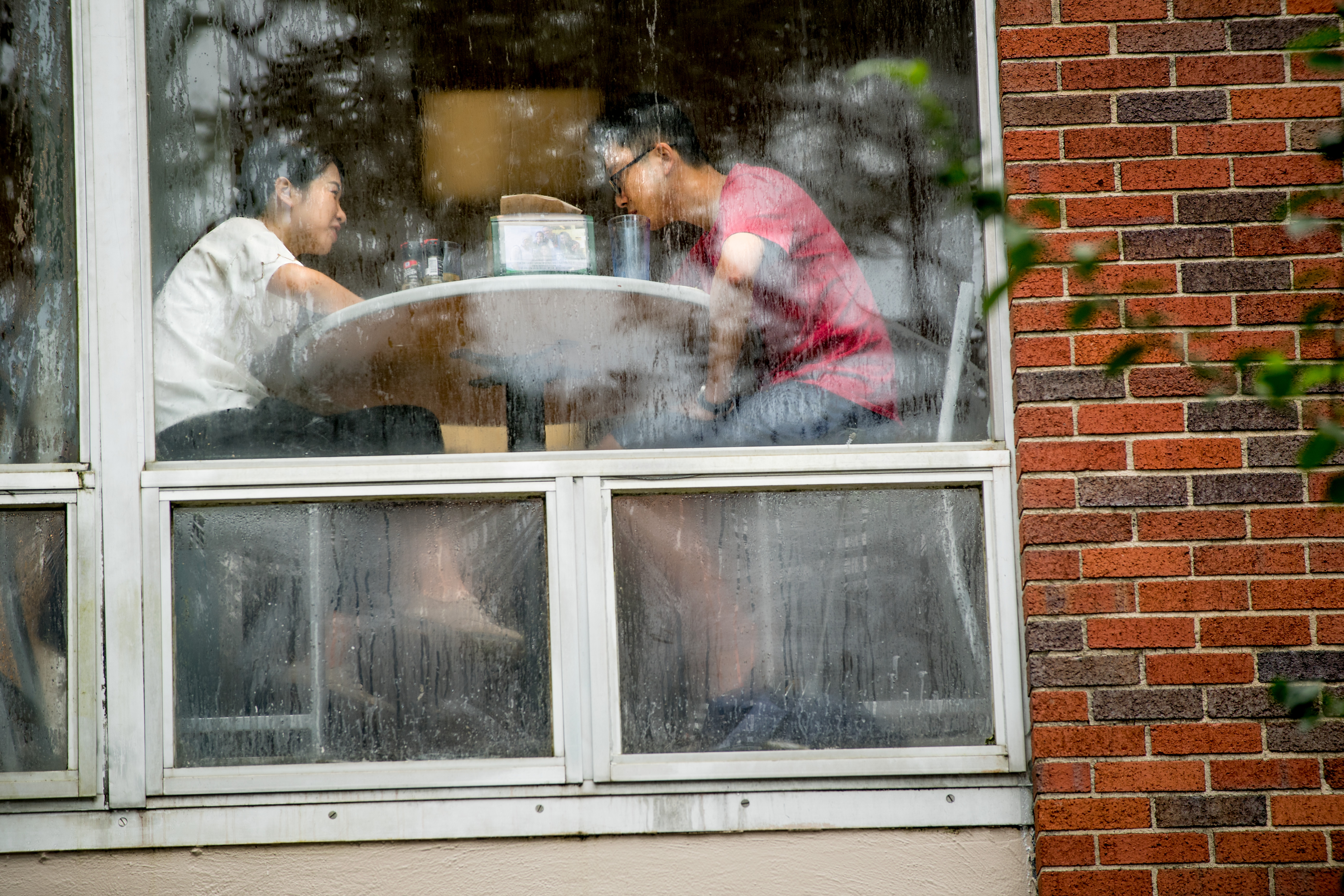 Two students at a lunch table on the other side of a window.