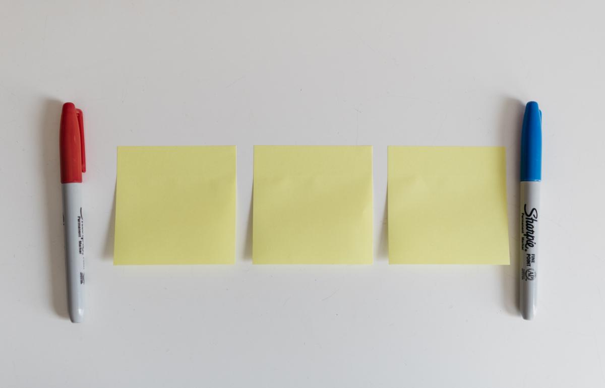 Three sticky notes lined up on a table with two markers.